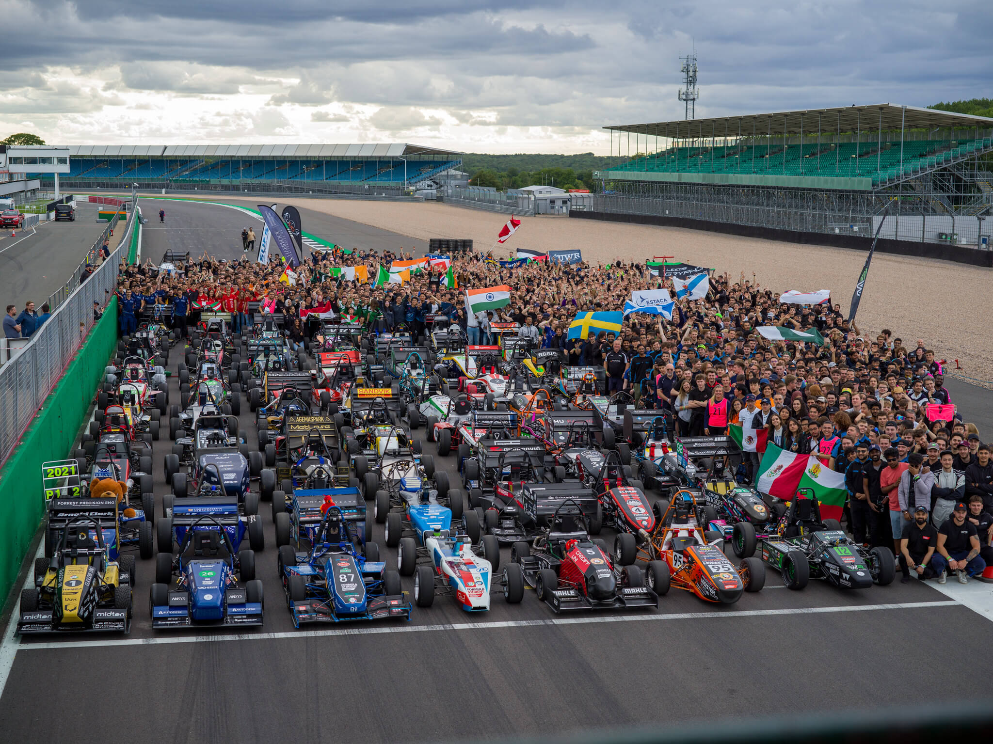 Racing cars lined up at starting line with crowds of Formula Students standing next to them